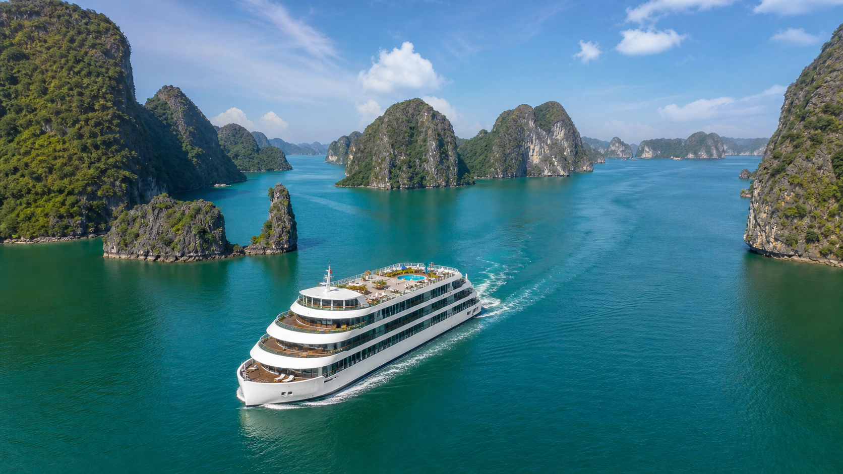 toàn cảnh một du thuyền 5 sao hiện đại màu trắng sang trọng đang lướt trên vịnh Hạ Long, nước xanh biếc, xung quanh là các dãy núi đá vôi hùng vĩ, góc chụp từ trên cao flycam