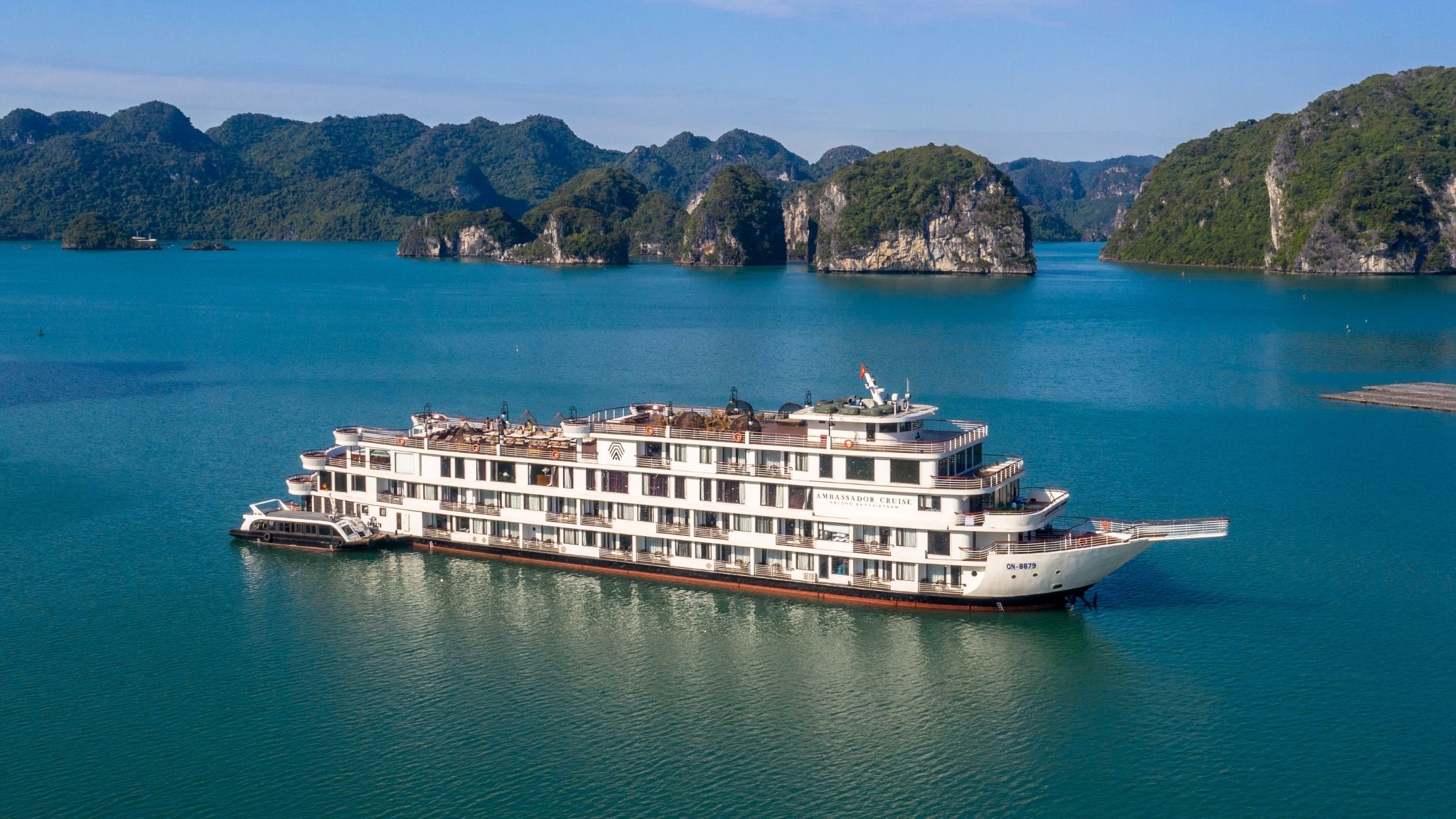 Du thuyền Ambassador 5 tầng màu trắng đang di chuyển trên Vịnh Hạ Long nhìn từ trên cao